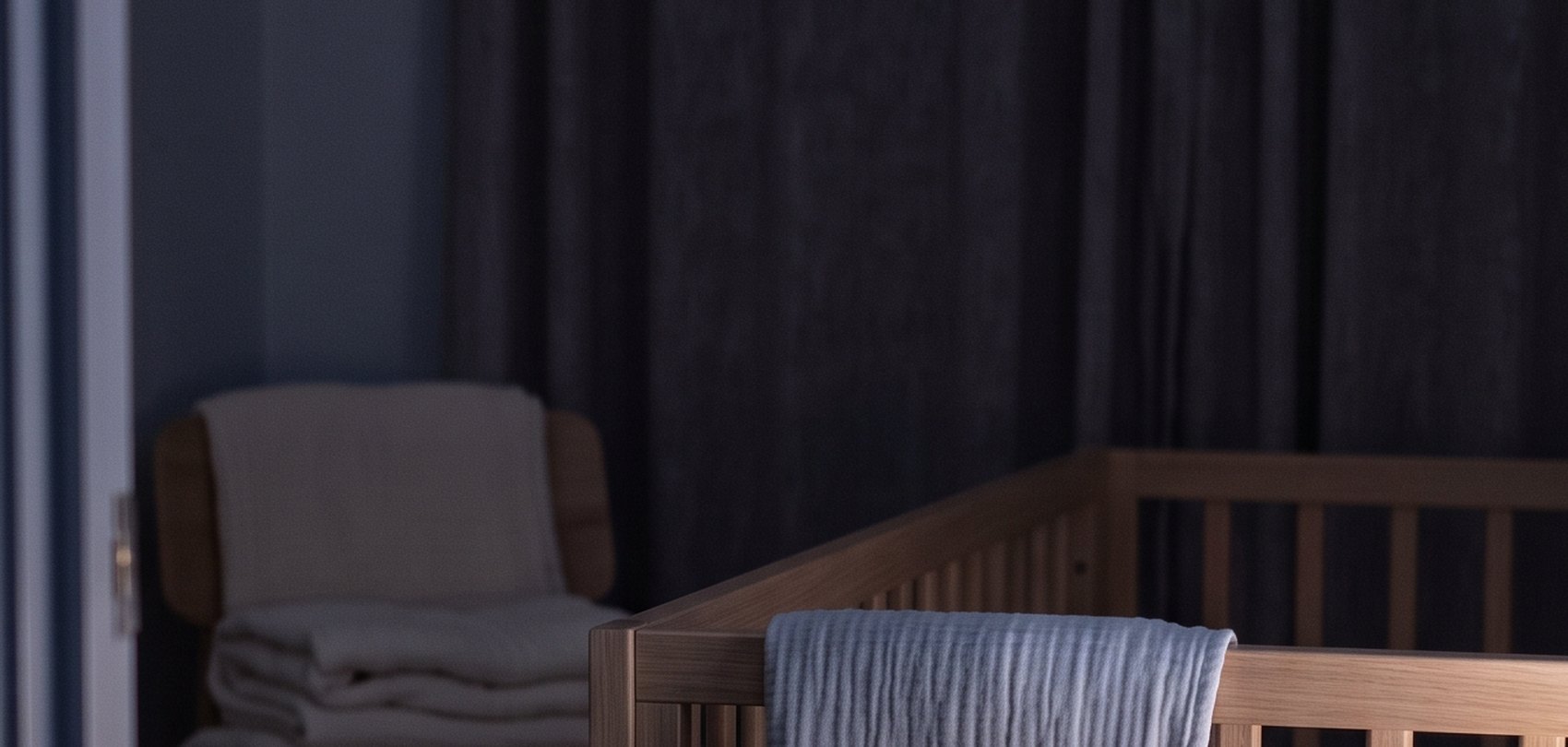 A dark nursery at night, a muslin cloth folded over the rail of a wooden cot